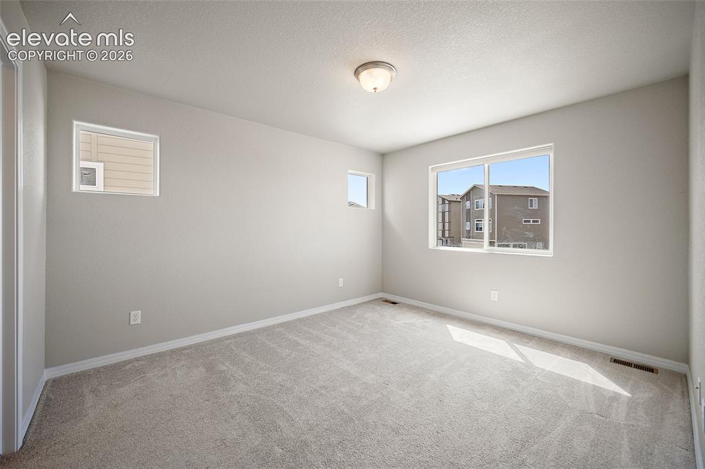 Image 25 of 40: Bright room featuring three windows, neutral-toned carpeting, and a flush-m