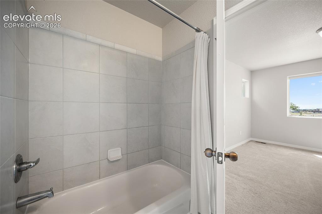 Image 28 of 40: Bathtub with light gray subway tile surround, chrome fixtures, and a shower