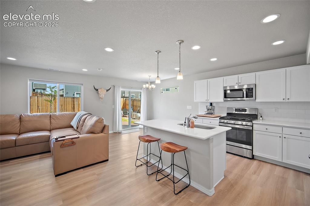Image 6 of 40: Open-concept kitchen featuring white shaker cabinetry, stainless steel appl
