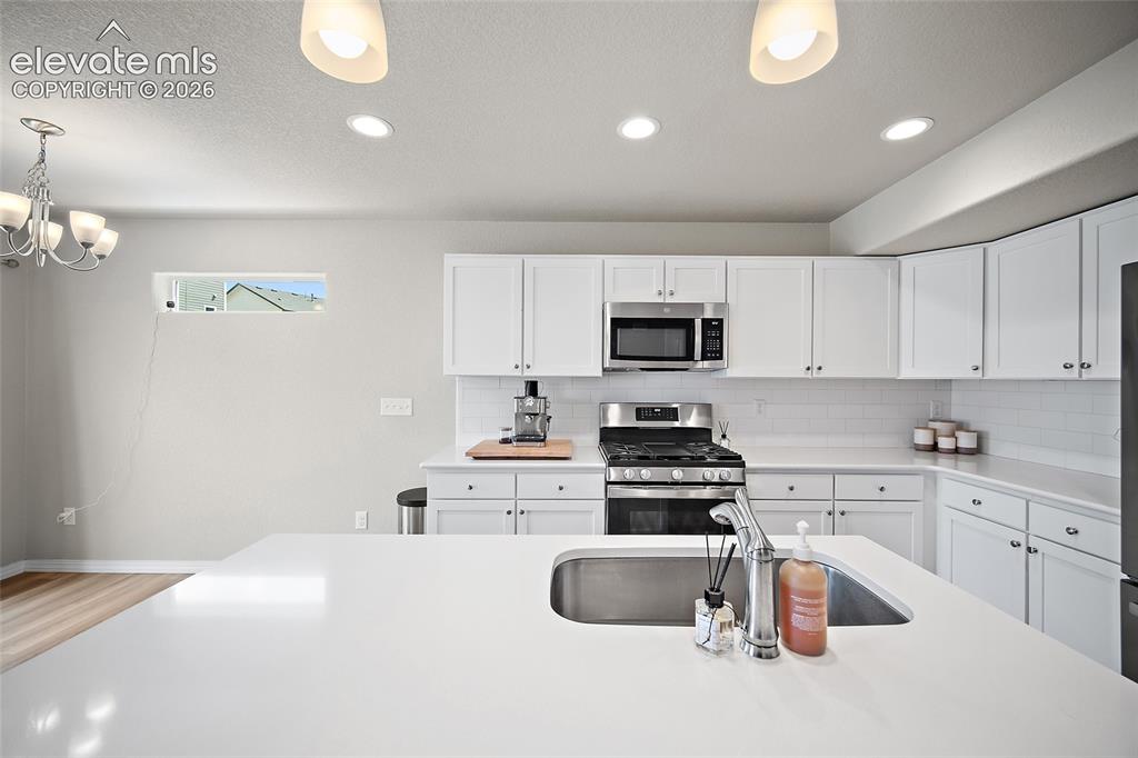 Image 7 of 40: Kitchen featuring white cabinetry, stainless steel appliances, a subway til