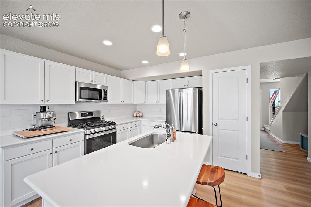 Image 8 of 40: Kitchen featuring white cabinetry, stainless steel appliances, a subway til