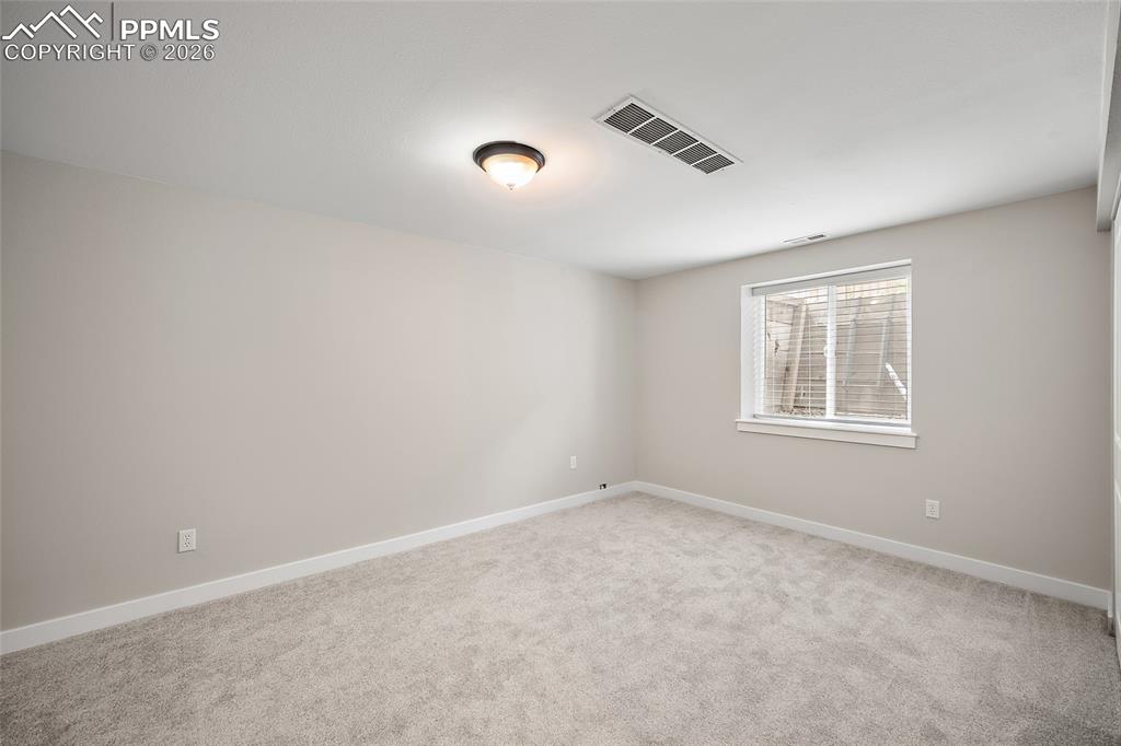 Image 17 of 36: Neutral-toned room featuring a single window with blinds, light gray carpet