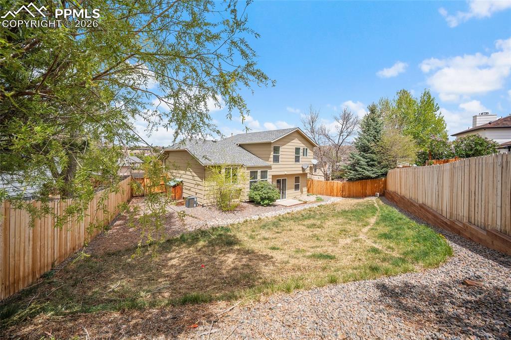 Image 30 of 36: Spacious fenced backyard featuring a patio area, rock landscaping, and matu
