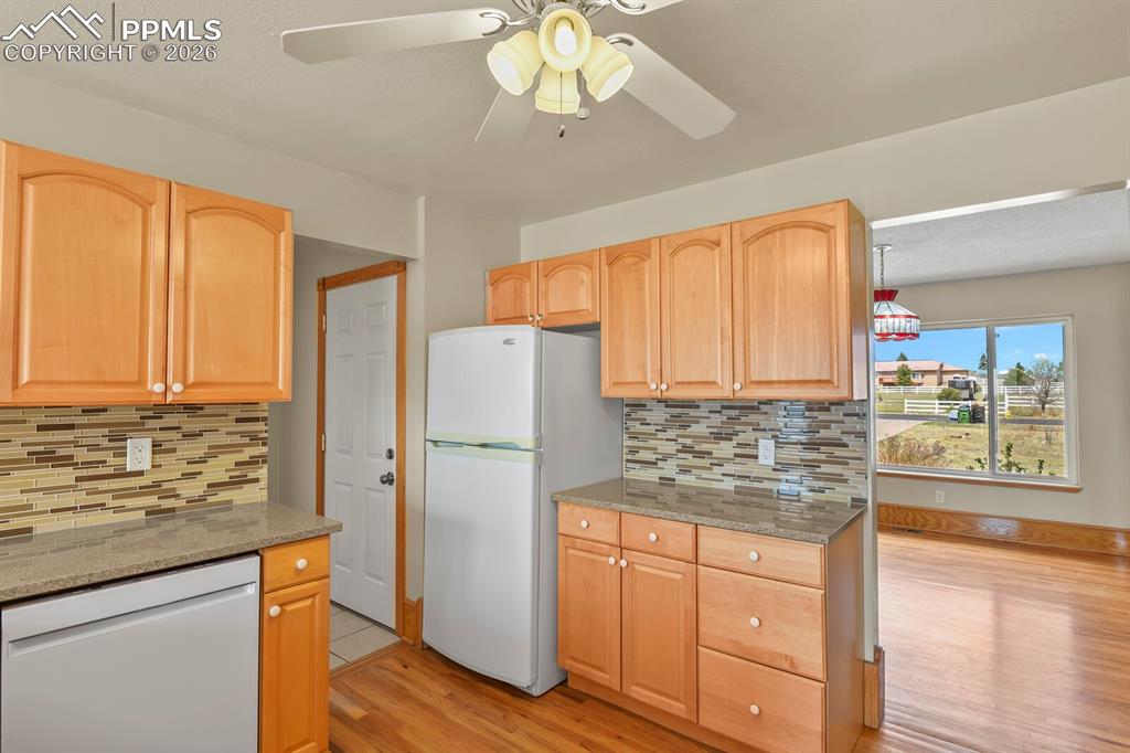 Image 12 of 37: Kitchen with white appliances, a ceiling fan, light stone counters, light w