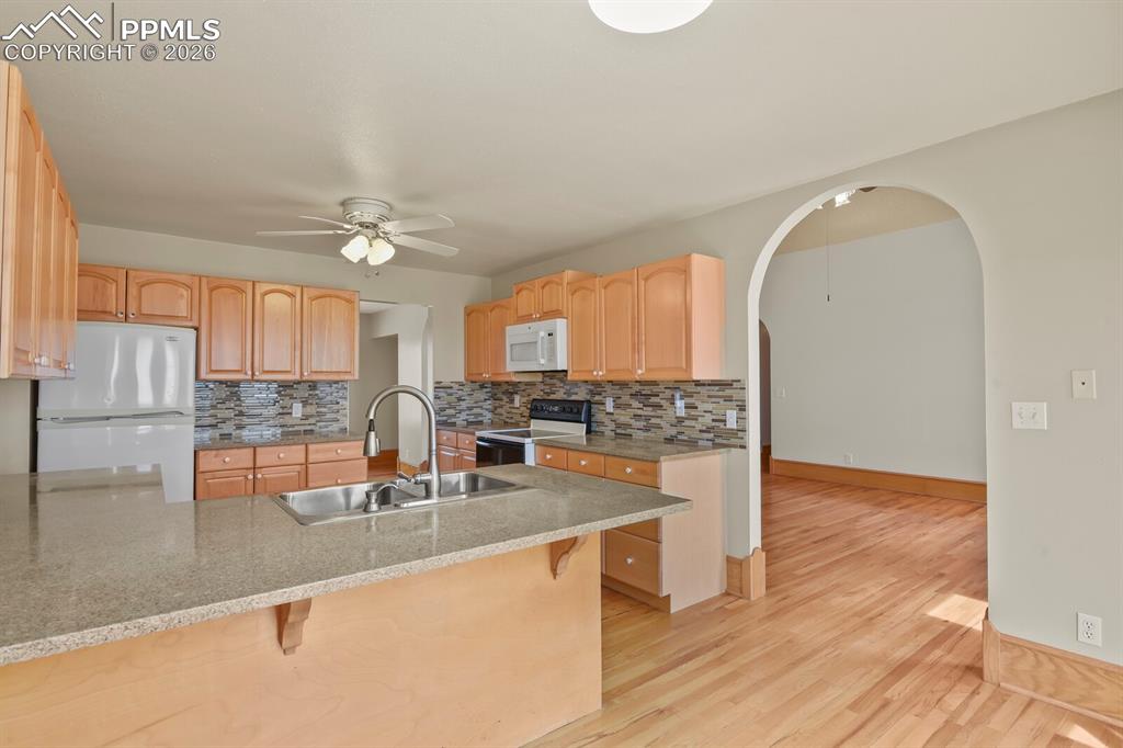 Image 9 of 37: Kitchen with a breakfast bar, ceiling fan, white appliances, light stone co