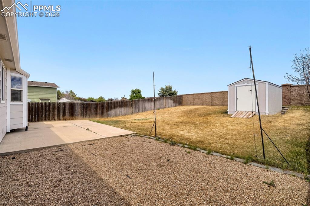 Image 29 of 32: Expansive backyard featuring a gravel patio, concrete pad, and a storage sh