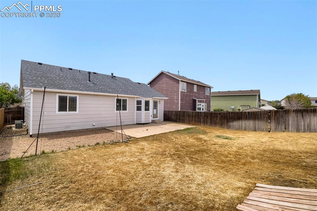 Image 32 of 32: Spacious backyard featuring a concrete patio, wood fencing, and a light-col