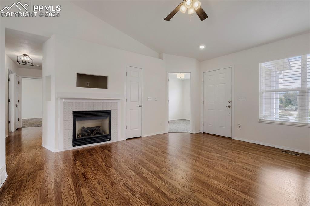 Image 8 of 32: Living area featuring wood-finish flooring, a fireplace with a tiled surrou