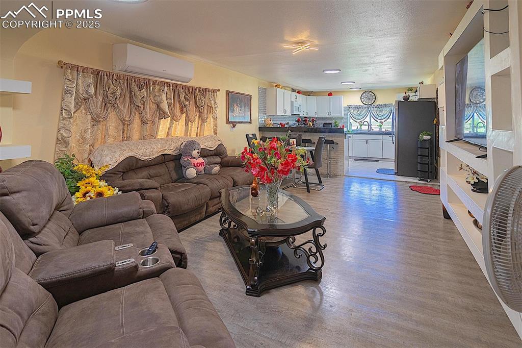 Image 23 of 38: Living room with an AC wall unit and light wood-type flooring