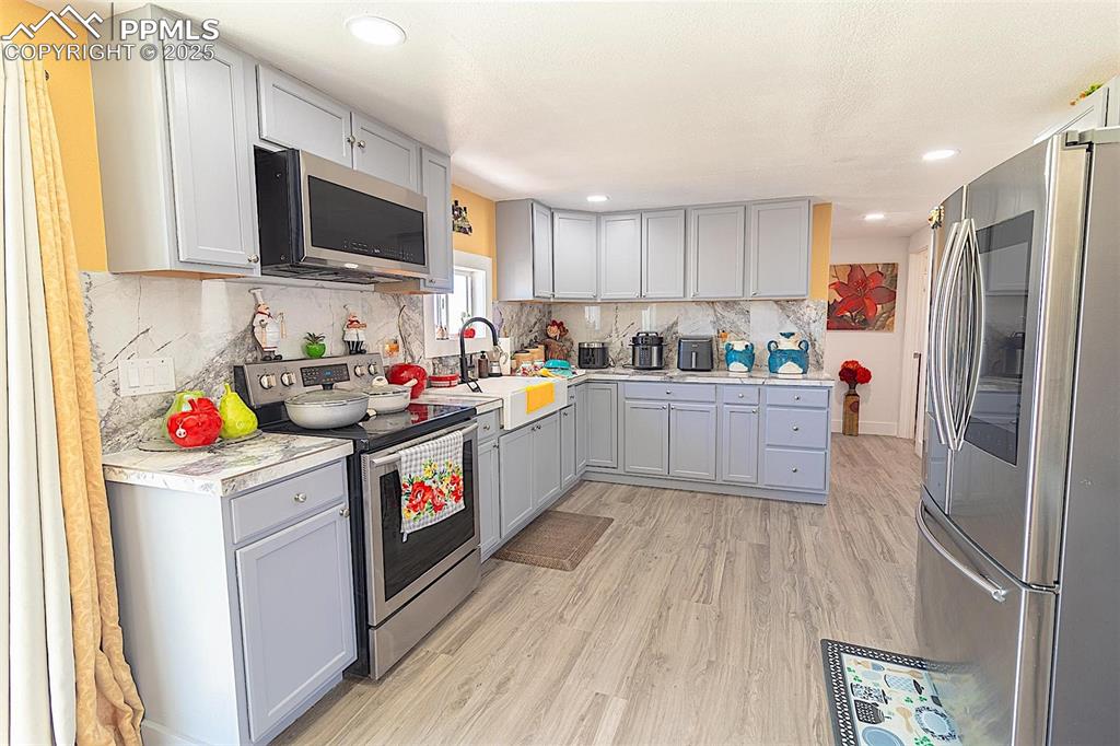 Image 28 of 38: Kitchen with stainless steel appliances, a sink, gray cabinetry, light wood