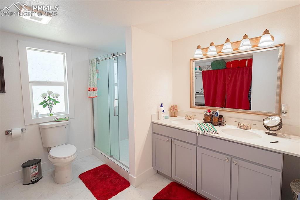 Image 34 of 38: Full bathroom with marble finish floors, a shower stall, double vanity, toi