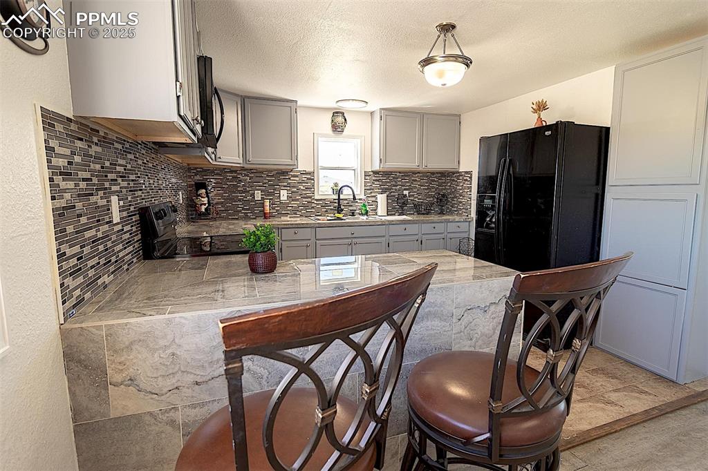Image 4 of 38: Kitchen featuring black appliances, a sink, decorative backsplash, light co