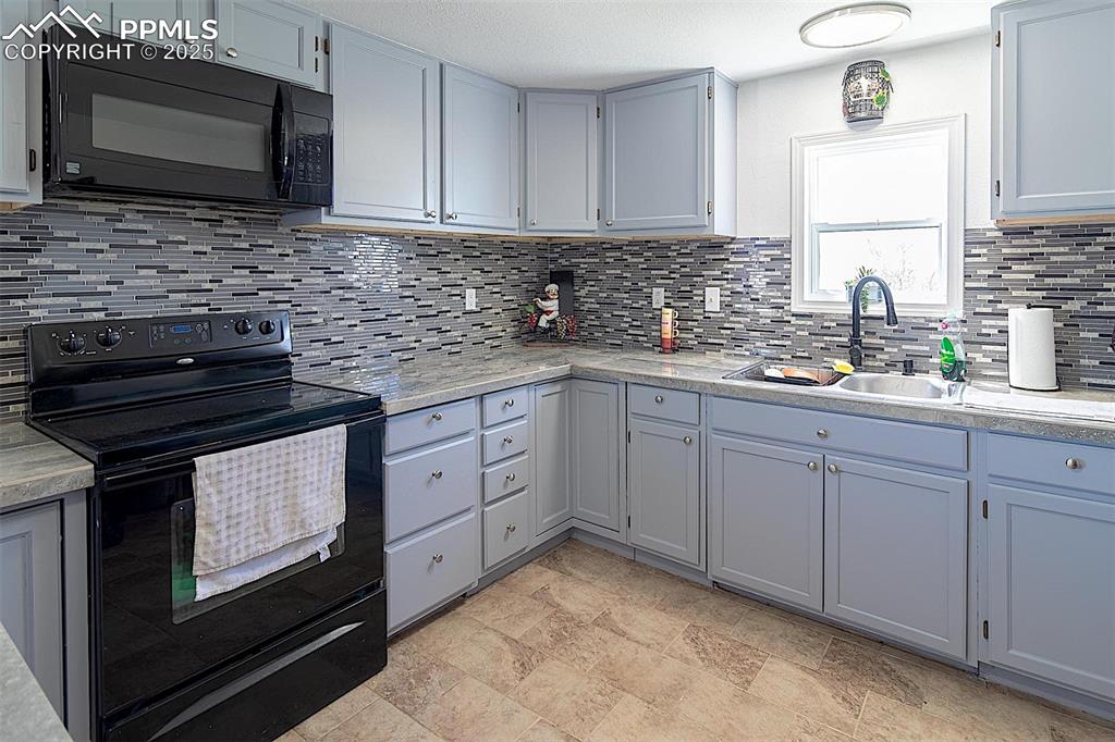 Image 5 of 38: Kitchen with black appliances, a sink, decorative backsplash, and light cou