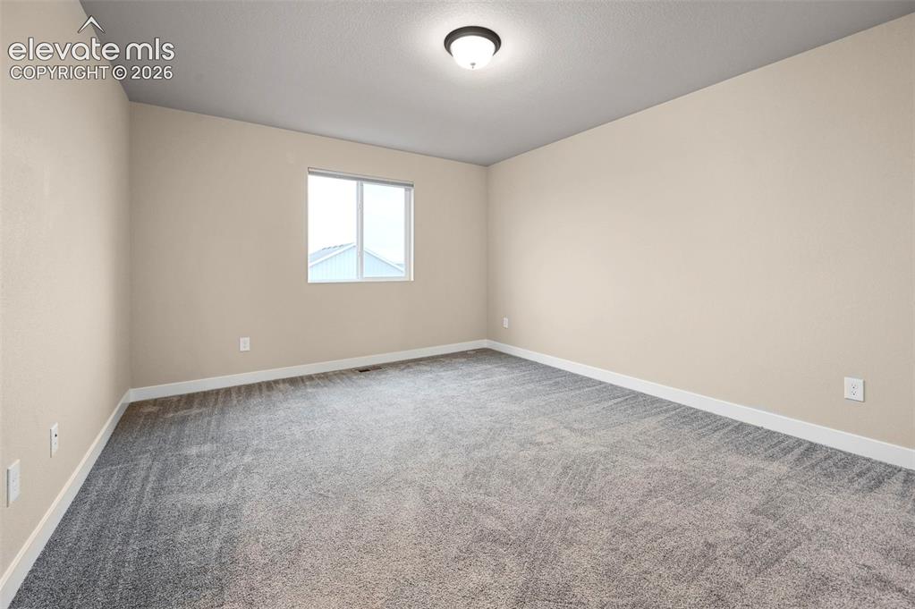 Image 14 of 28: Neutral-toned room featuring light beige walls and grey patterned carpeting