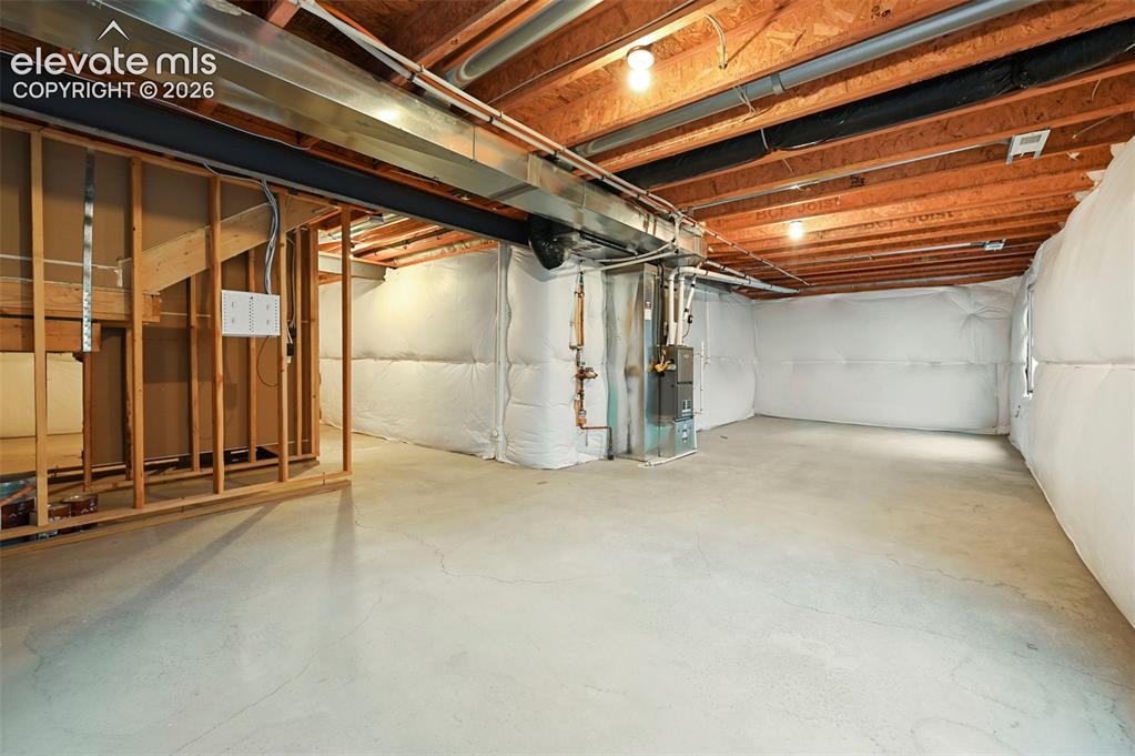 Image 24 of 28: Unfinished basement featuring exposed wood joists, concrete flooring, and i