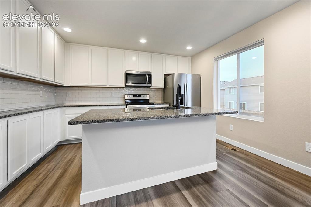 Image 4 of 25: Modern kitchen featuring white cabinetry, granite-style countertops, stainl