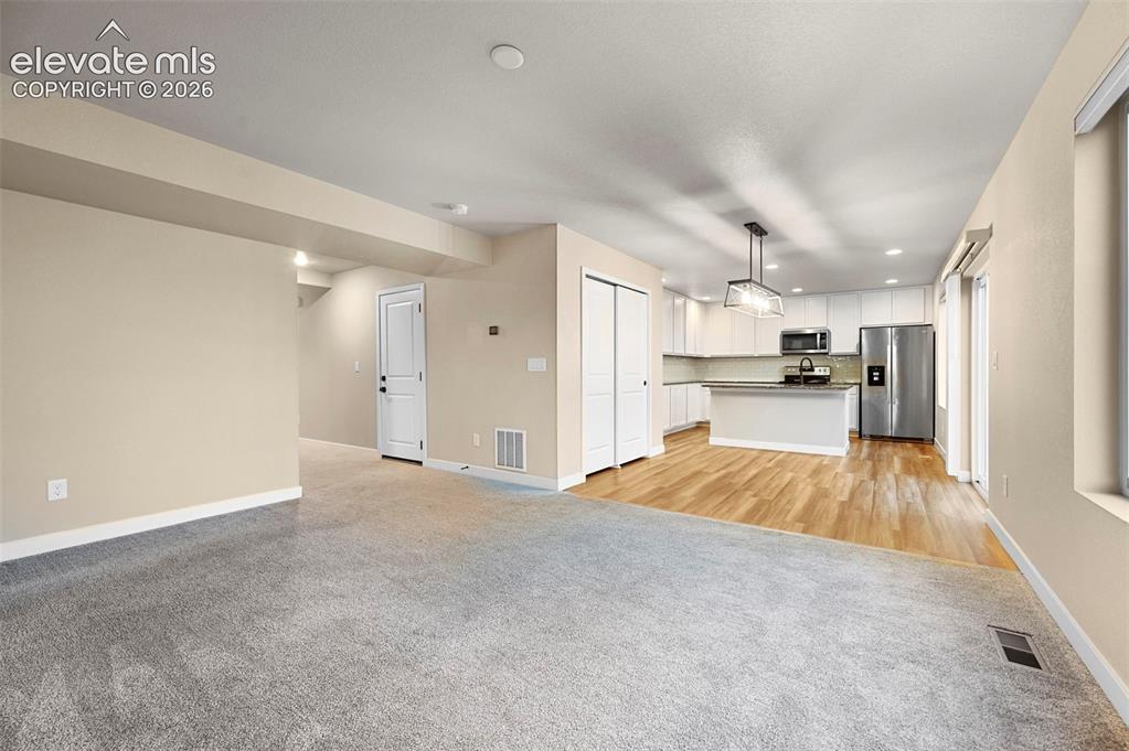 Image 9 of 28: Open-concept living space featuring light gray carpeting and wood-finish fl