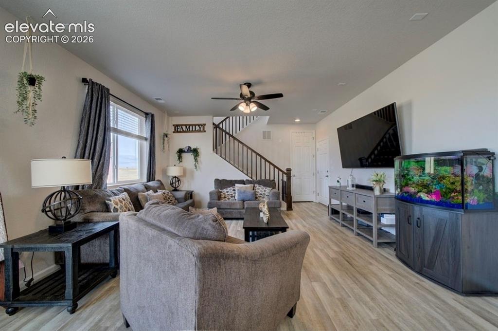 Image 14 of 34: Laminate wood-finish flooring, staircase with dark handrail, ceiling fan wi