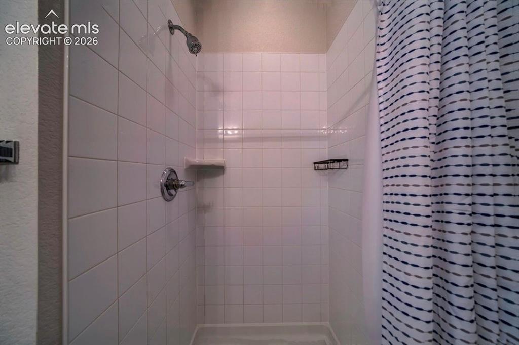 Image 32 of 34: Shower stall with white square tiling, chrome showerhead and control, and b