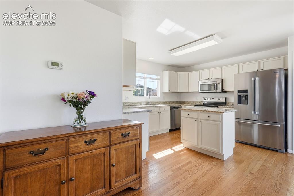 Image 12 of 37: Kitchen featuring light wood-finish flooring, white cabinetry, a central is