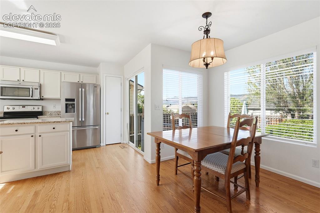 Image 14 of 37: Bright kitchen dining area featuring light wood-finish flooring, white cabi