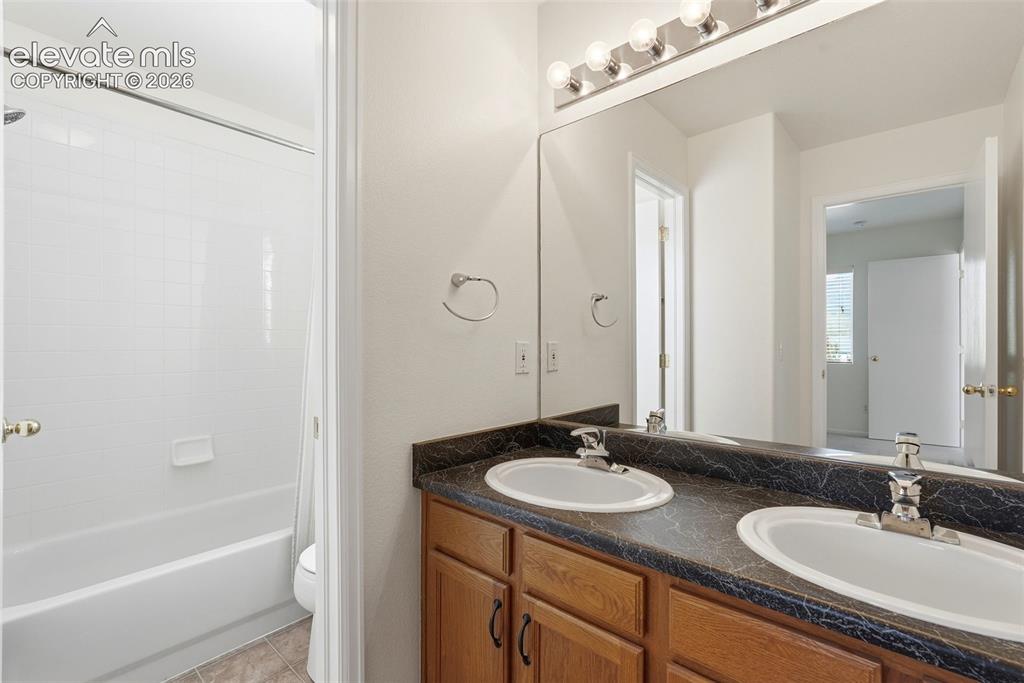 Image 21 of 37: Bathroom featuring a dual vanity with a dark countertop and wood-finish cab