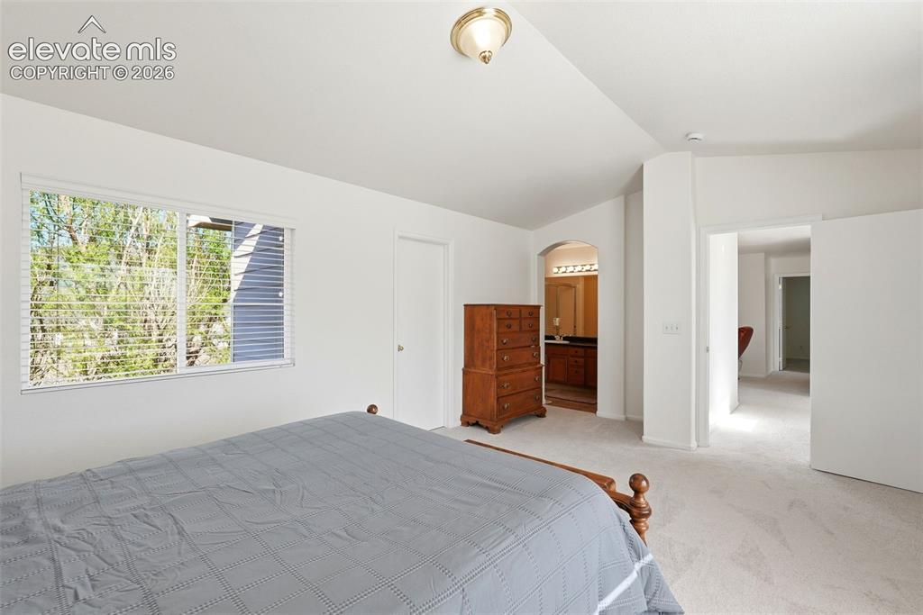 Image 26 of 37: Carpeted bedroom with a large window, a vaulted ceiling, and an arched door