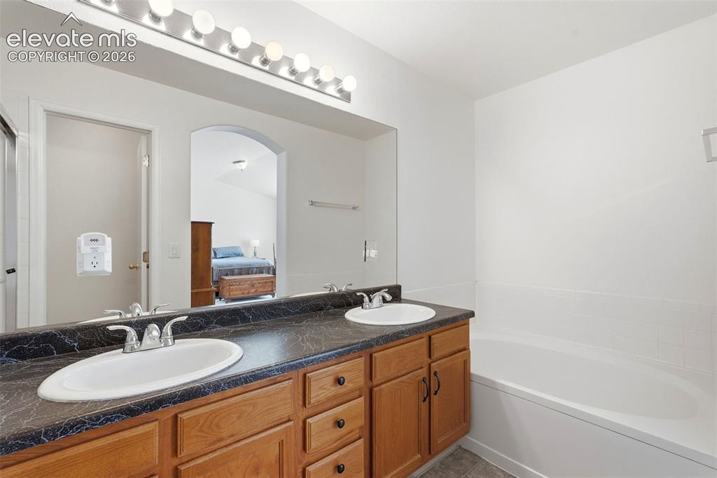 Image 28 of 37: Dual vanity with wood-finish cabinetry and a dark countertop