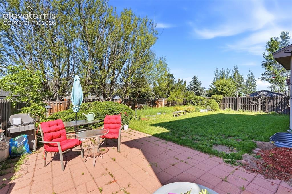 Image 29 of 37: Spacious backyard featuring a large paved patio, expansive lawn area, matur