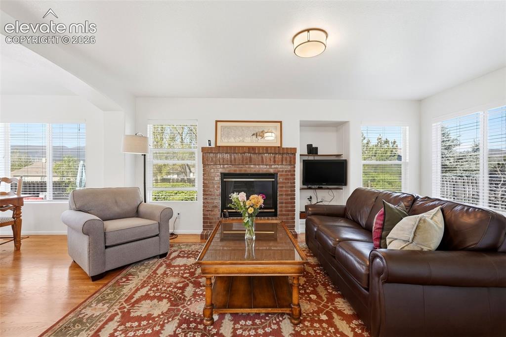 Image 3 of 37: Spacious living area featuring a brick-surround fireplace, built-in shelvin