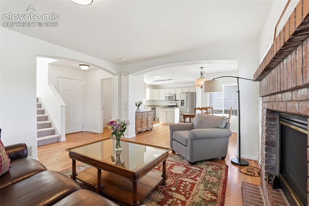 Image 5 of 37: Open-concept living area featuring a brick fireplace, wood-finish flooring,