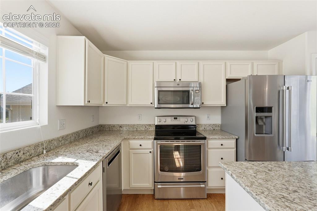 Image 9 of 37: Modern kitchen featuring white cabinetry, light-toned granite countertops,