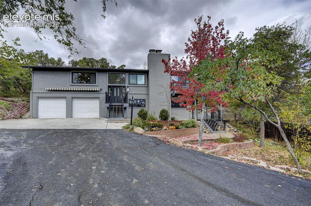 Caption: Split-level exterior featuring a painted brick facade, two-car garage with white paneled doors, tier