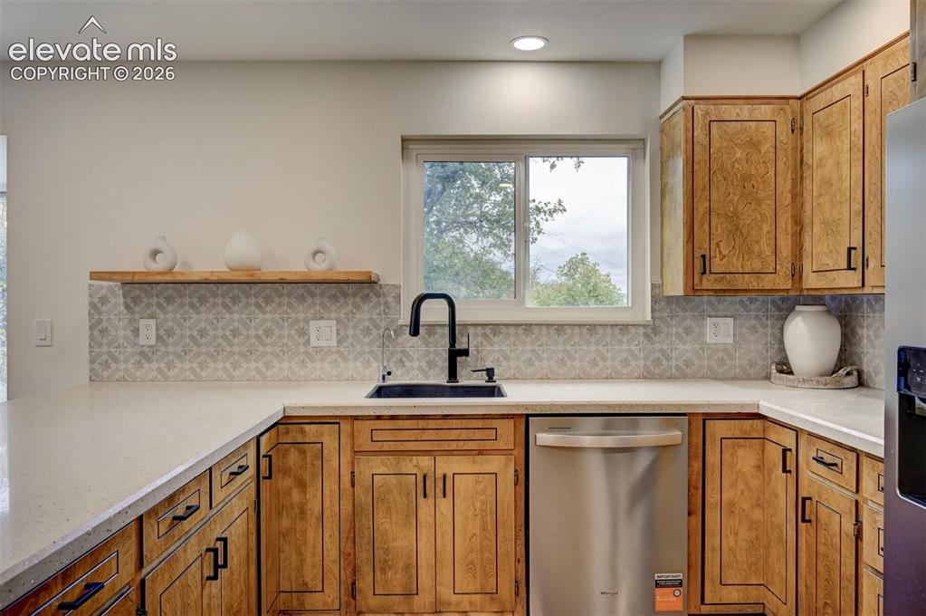 Image 17 of 50: Kitchen featuring wood cabinetry with matte black hardware, stone-finish co