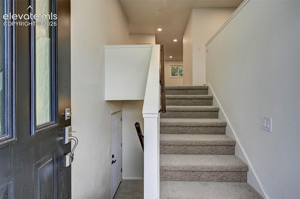 Image 38 of 50: Entryway featuring a dark-toned door with glass paneling, carpeted staircas