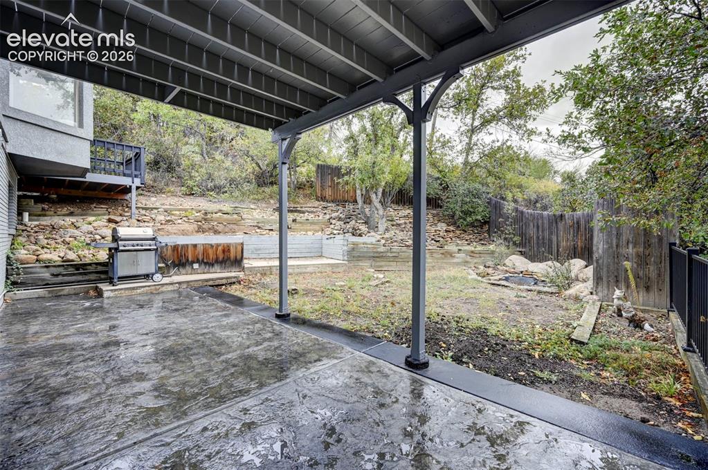 Image 46 of 50: Covered concrete patio featuring structural support columns, tiered stone r