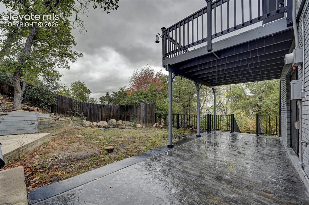 Image 48 of 50: Covered concrete patio featuring a tiered wood-plank deck, black metal rail