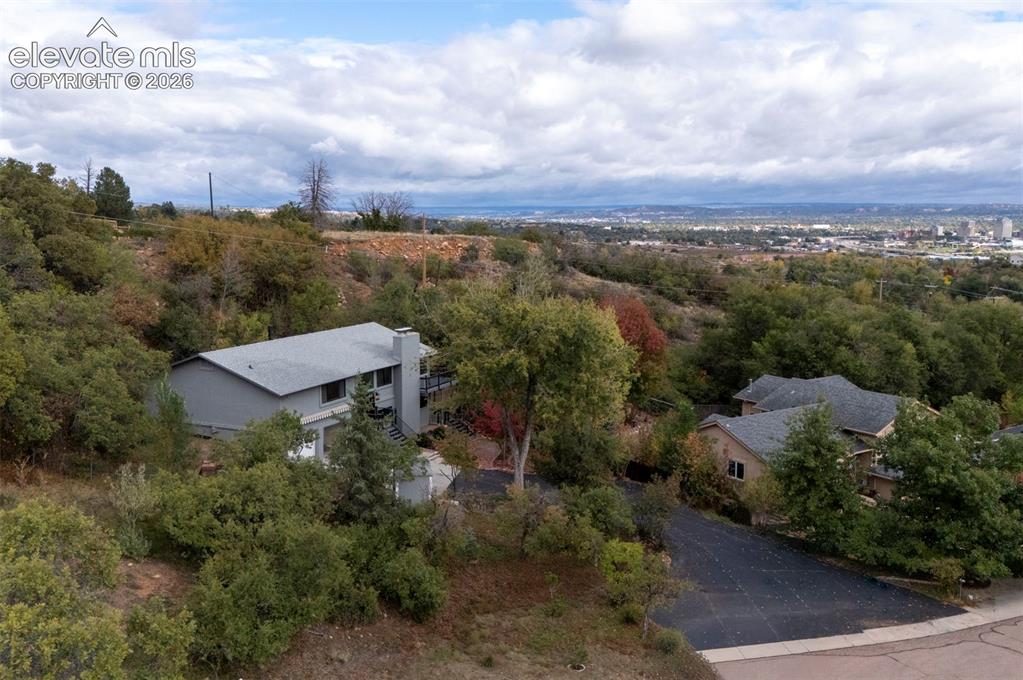 Image 5 of 50: Elevated hillside property featuring an asphalt driveway, mature trees, mul