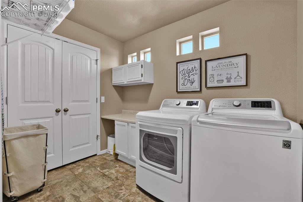 Image 19 of 50: Clothes washing area featuring washing machine and clothes dryer, cabinet s