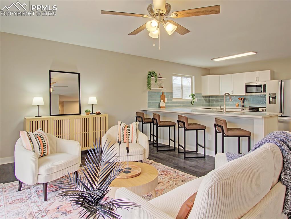 Image 14 of 26: Living room with a ceiling fan and dark wood-style flooring