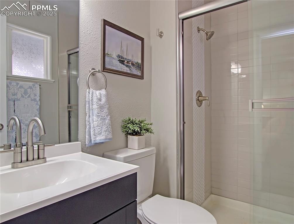 Image 22 of 26: Full bathroom featuring a shower stall, vanity, and a textured wall