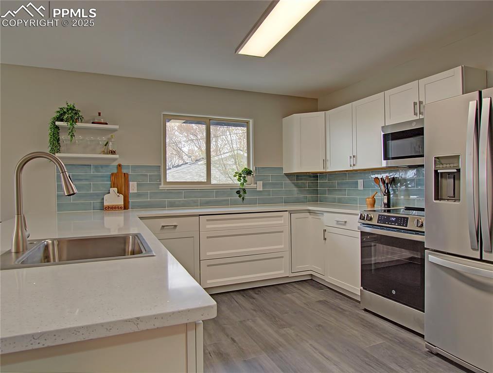 Image 9 of 26: Kitchen featuring stainless steel appliances, white cabinets, light stone c