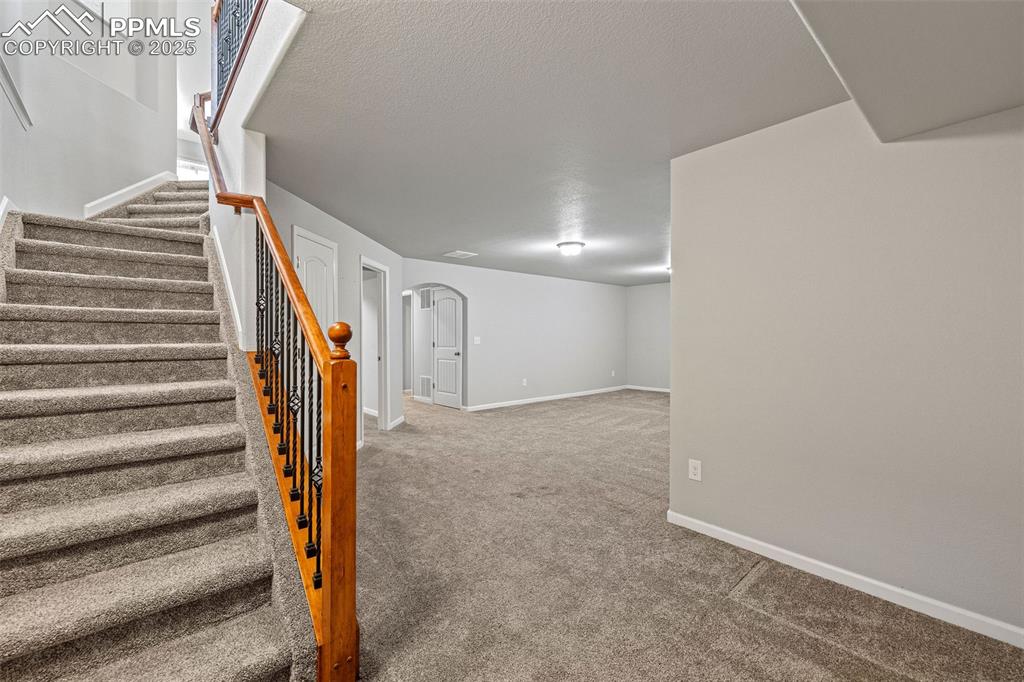 Image 23 of 42: Basement featuring arched walkways, light carpet, stairway, and a textured