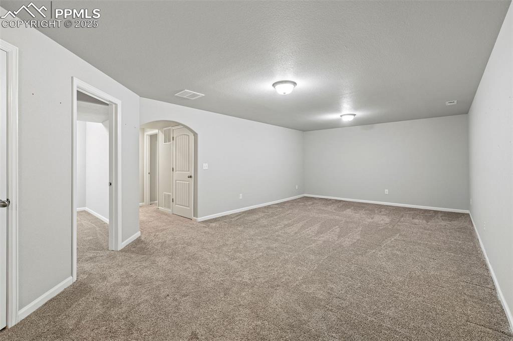 Image 24 of 42: Spare room with arched walkways, light carpet, and a textured ceiling