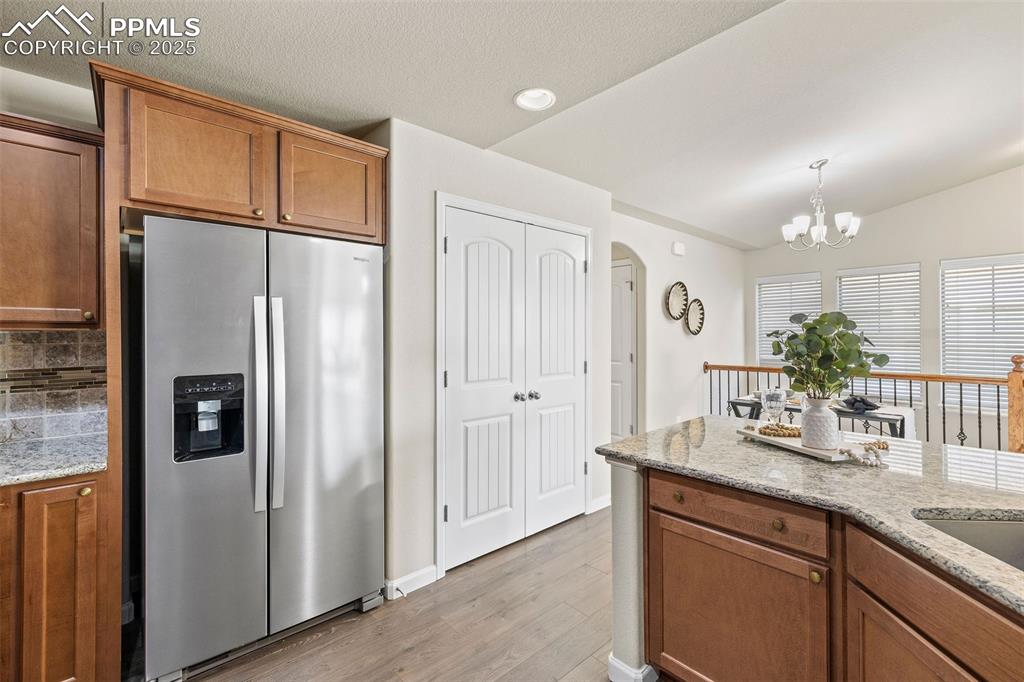 Image 8 of 42: Kitchen featuring brown cabinets, stainless steel fridge, light stone count
