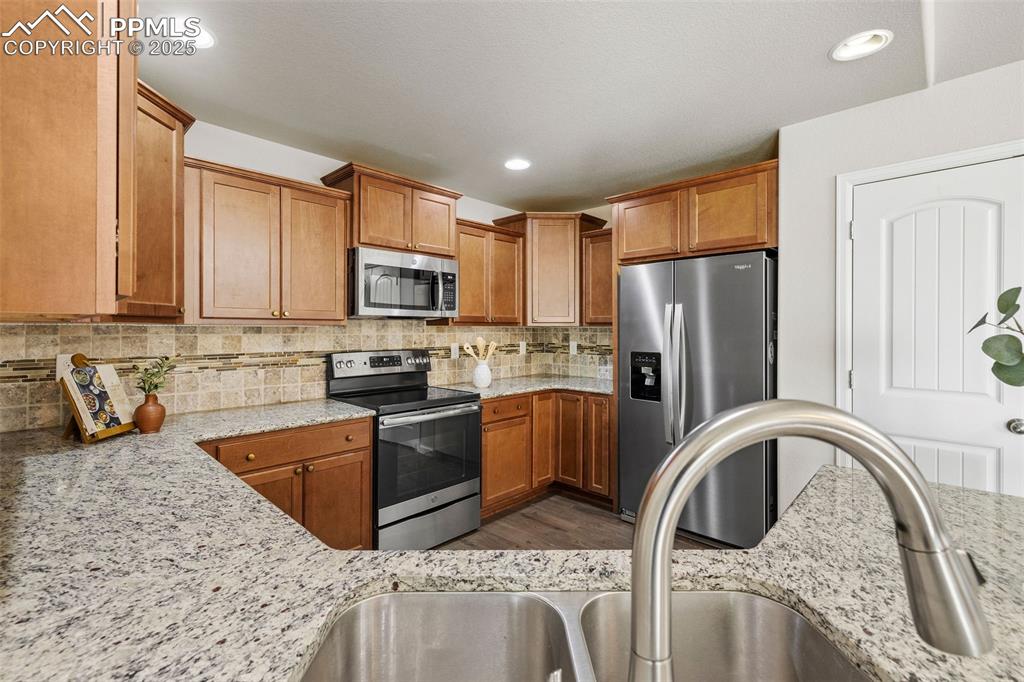 Image 9 of 42: Kitchen with appliances with stainless steel finishes, brown cabinets, ligh