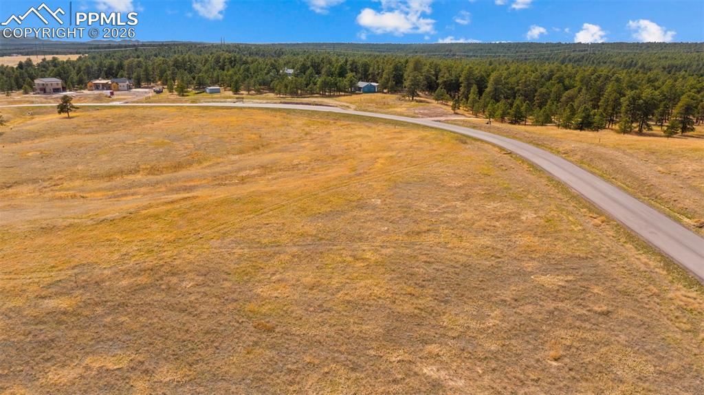Image 3 of 17: Expansive open land featuring a paved road, scattered mature trees, and dis