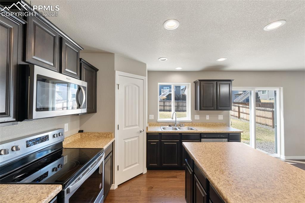 Image 22 of 25: Kitchen with stainless steel appliances, a textured ceiling, dark wood-styl