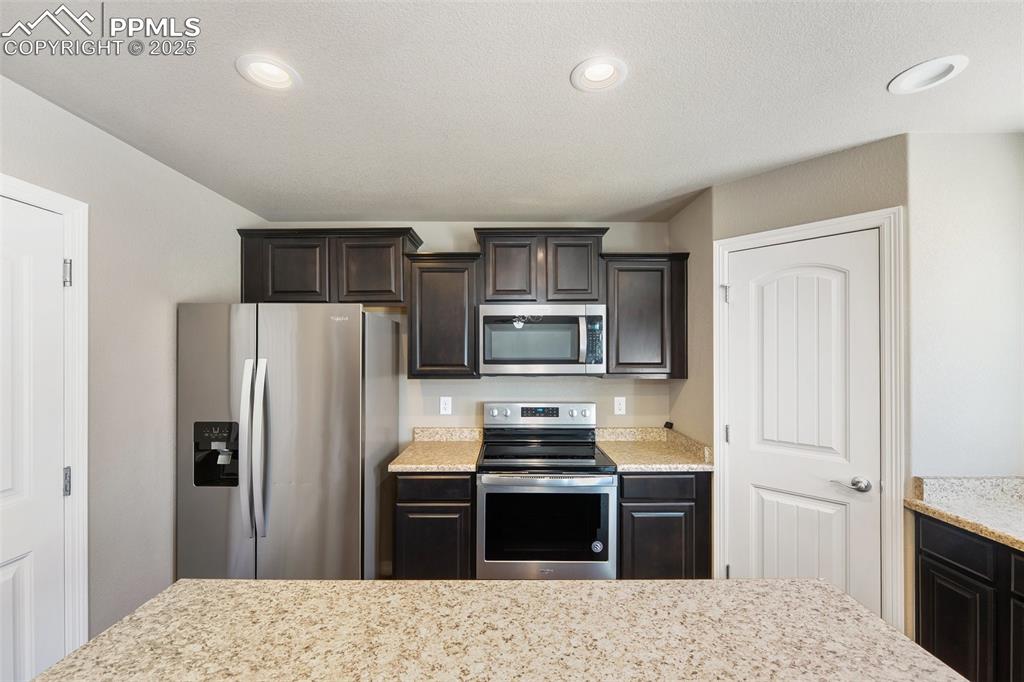 Image 24 of 25: Kitchen featuring stainless steel appliances, dark brown cabinets, recessed