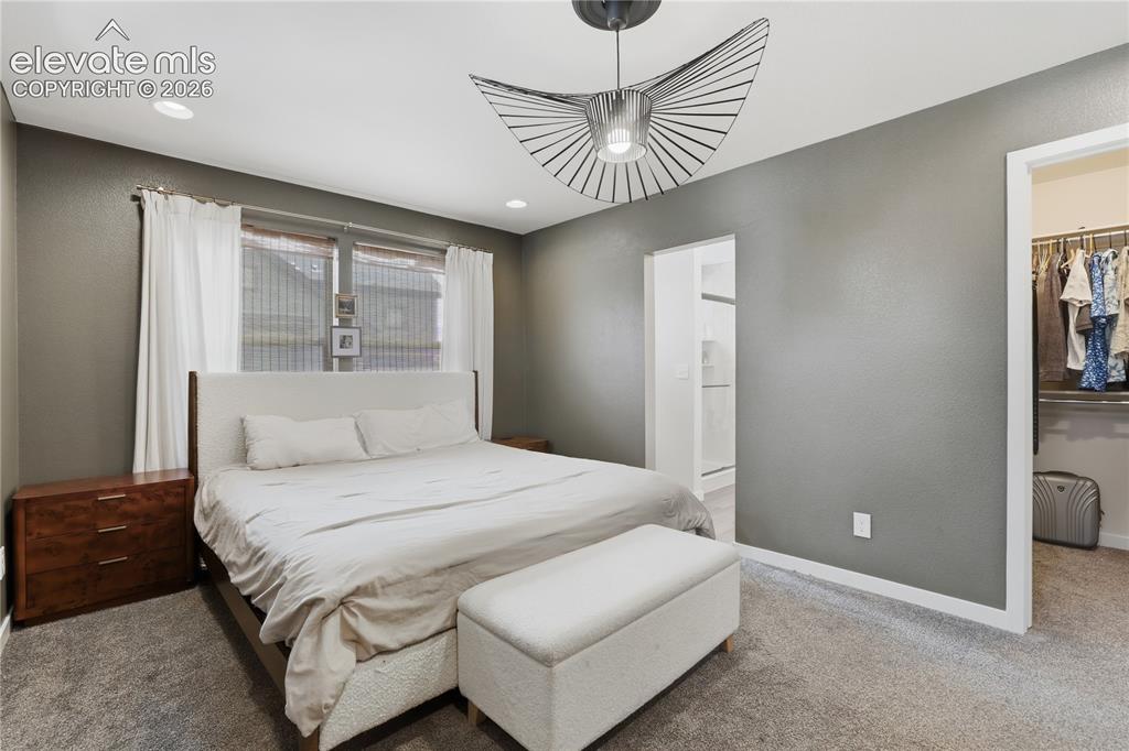 Image 20 of 48: Carpeted bedroom with a window featuring white curtains and horizontal blin